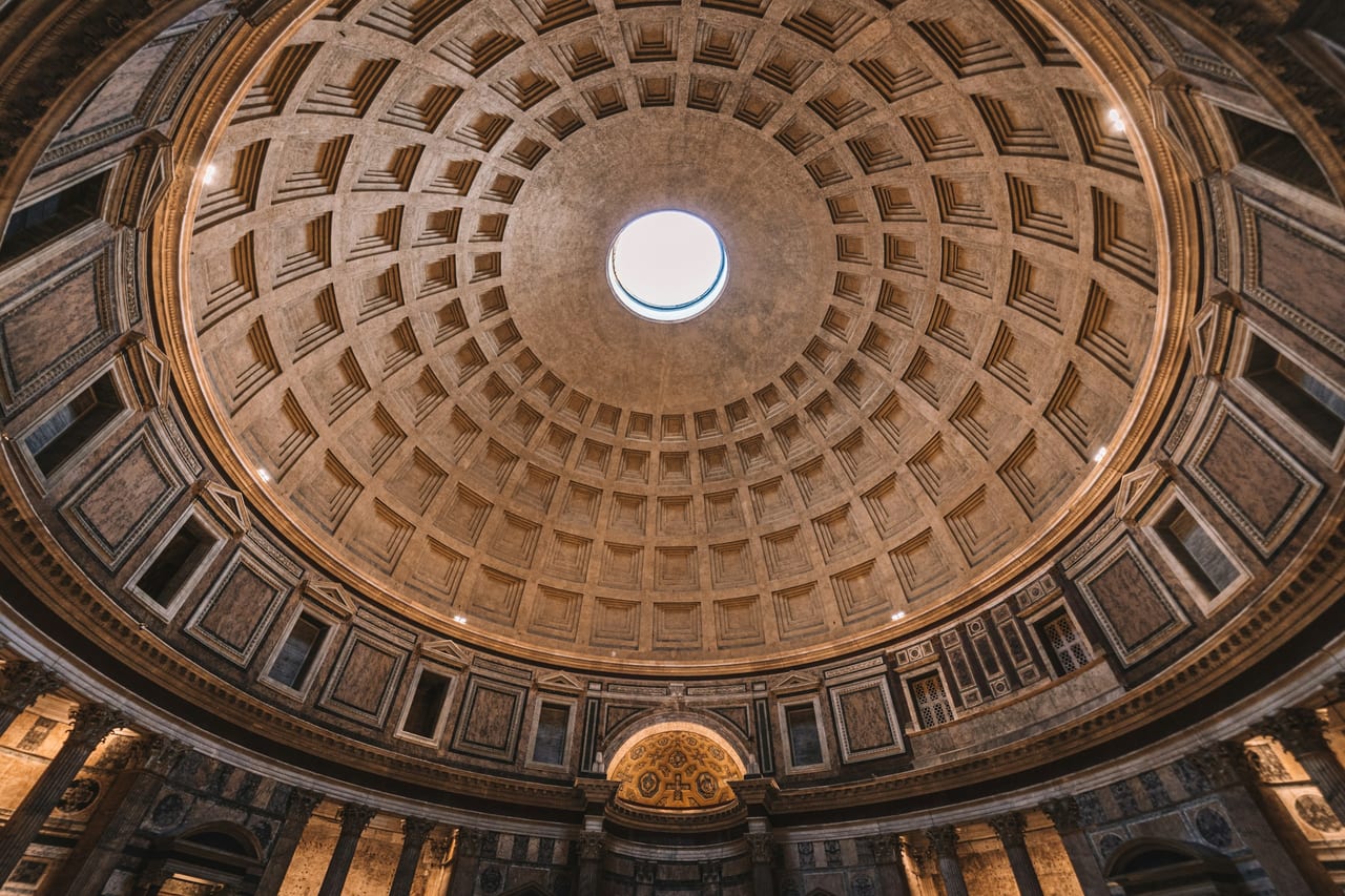 The Pantheon's coffered concrete dome curves up to the open oculus, a single shaft of daylight falling through it.