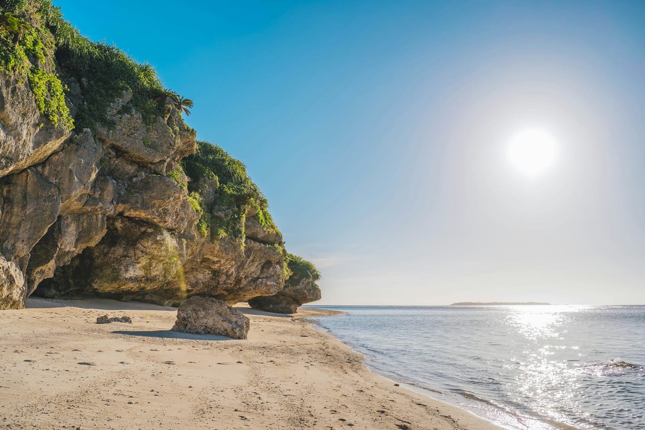 A sandy beach curves beneath a rocky, vegetated sea cliff.